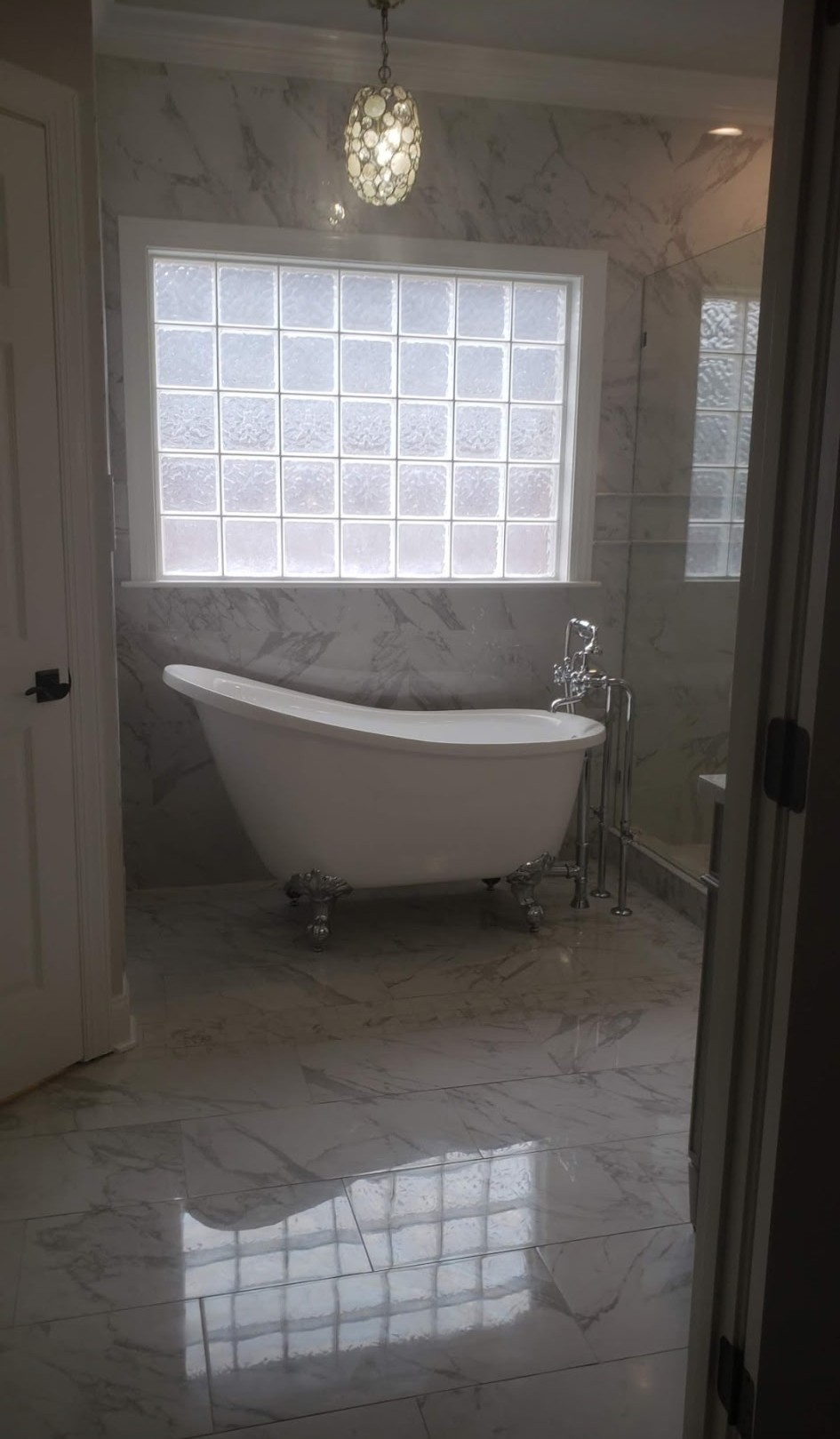 Freestanding clawfoot tub beneath a glass block window in a marble bathroom